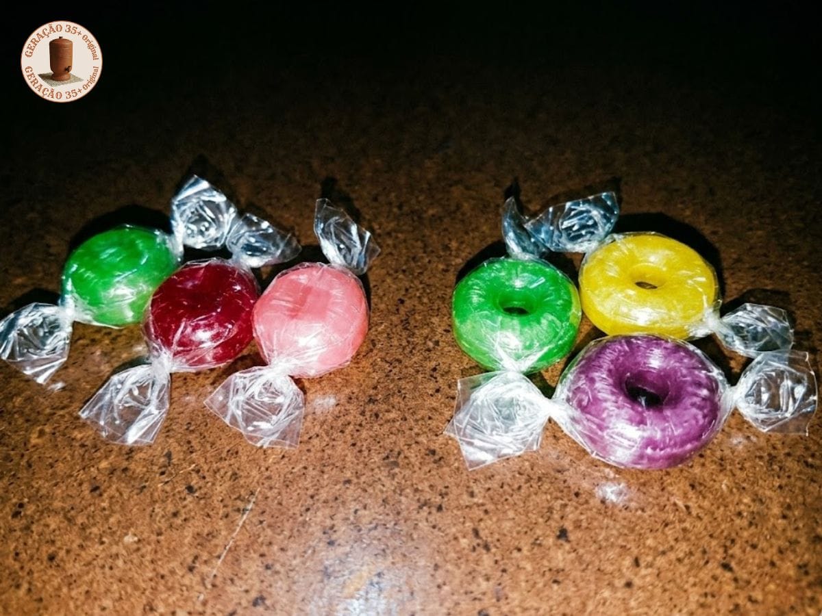 Fotografia em estilo vintage de bala soft colorida (verde, vermelha e amarela) com e sem furo central, dispostas sobre superfície escura com iluminação de flash direto.