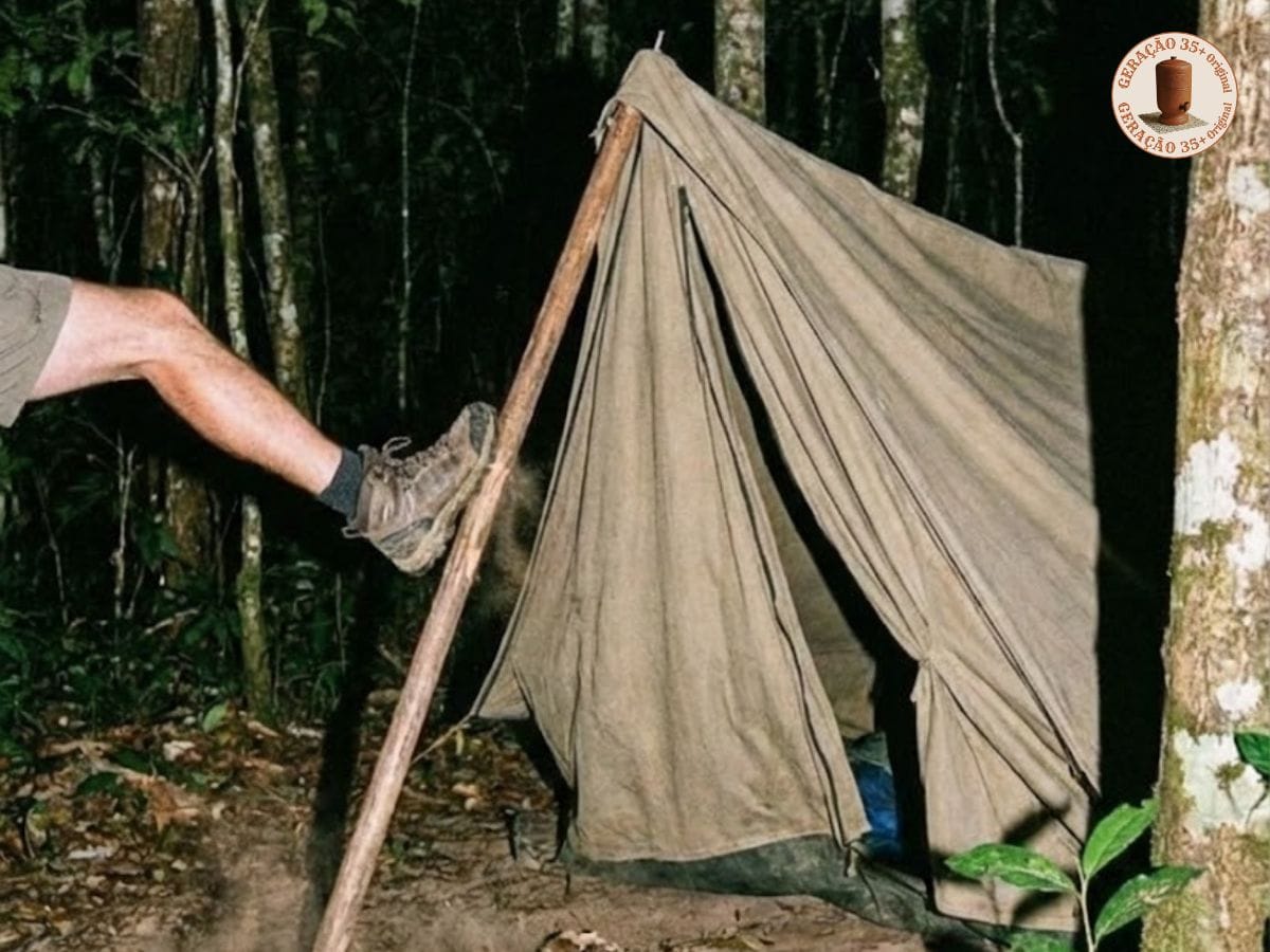 Foto dramática em close-up de uma pessoa calçando uma bota de caminhada no momento exato de chutar o pau da barraca de lona antiga e rústica, fazendo-a desmoronar. A cena ocorre em uma floresta escura à noite. O logotipo circular vermelho e dourado no canto superior direito diz "GERAÇÃO 35+ ORIGINAL"